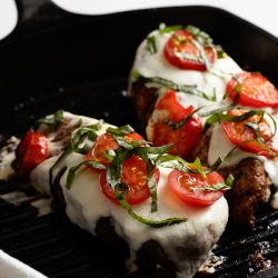 Stovetop Grilled Chicken Caprese features tender chicken breasts topped with melted mozzarella, juicy sliced tomatoes, and fragrant chopped basil, all elegantly presented in a black skillet.