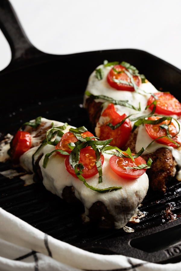 Stovetop Grilled Chicken Caprese features tender chicken breasts topped with melted mozzarella, juicy sliced tomatoes, and fragrant chopped basil, all elegantly presented in a black skillet.