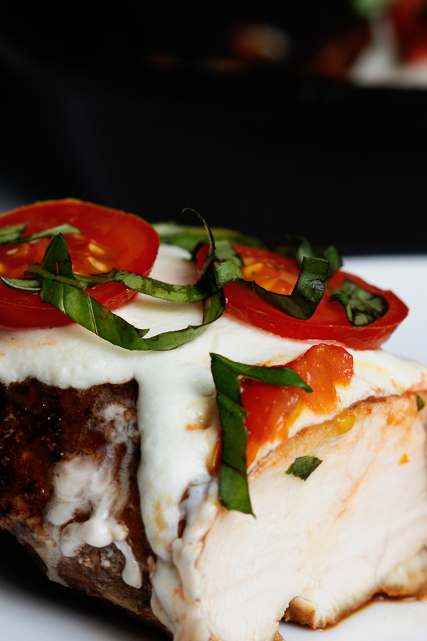 Close-up of meat topped with melted cheese, sliced tomatoes, and fresh basil for a delicious Caprese flavor delight.