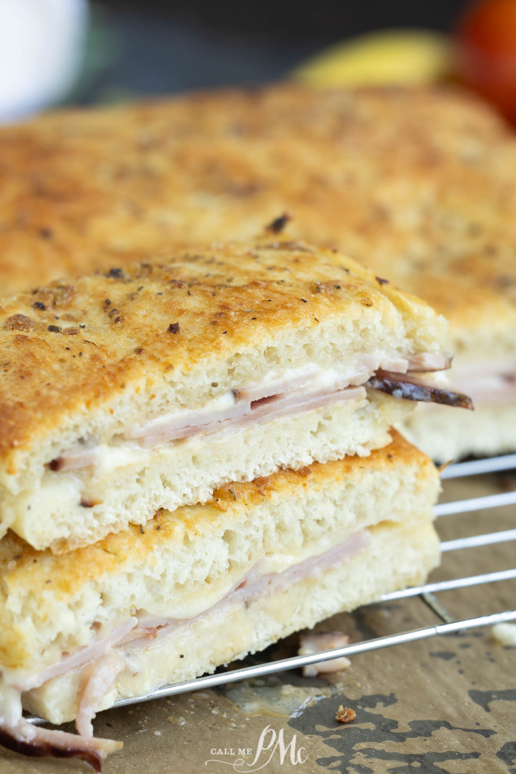 Close-up of a sliced sandwich showcasing layers of meat and cheese between thick, crusty bread. The sandwich is resting on a cooling rack.