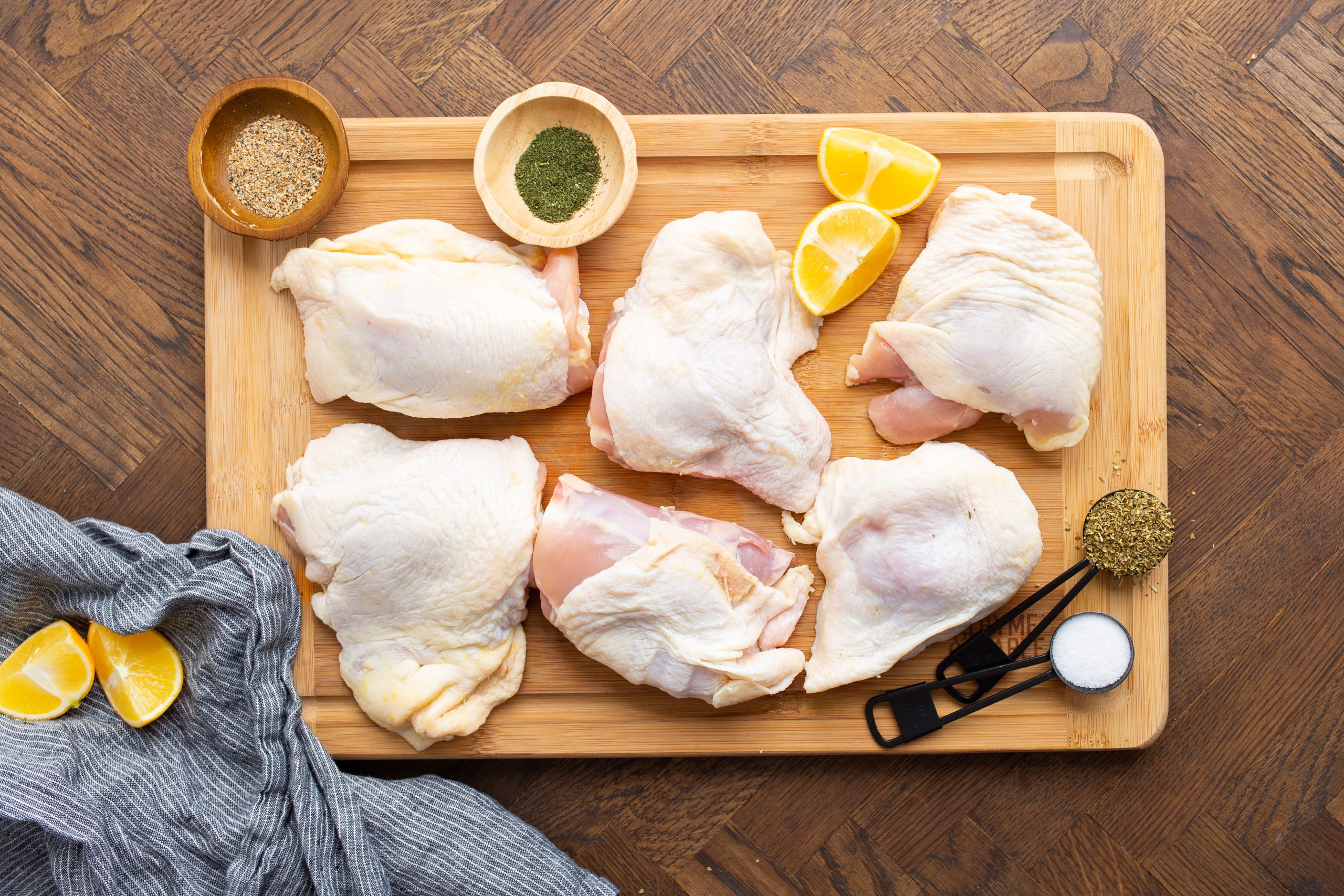 Raw chicken on a cutting board with lemon wedges.