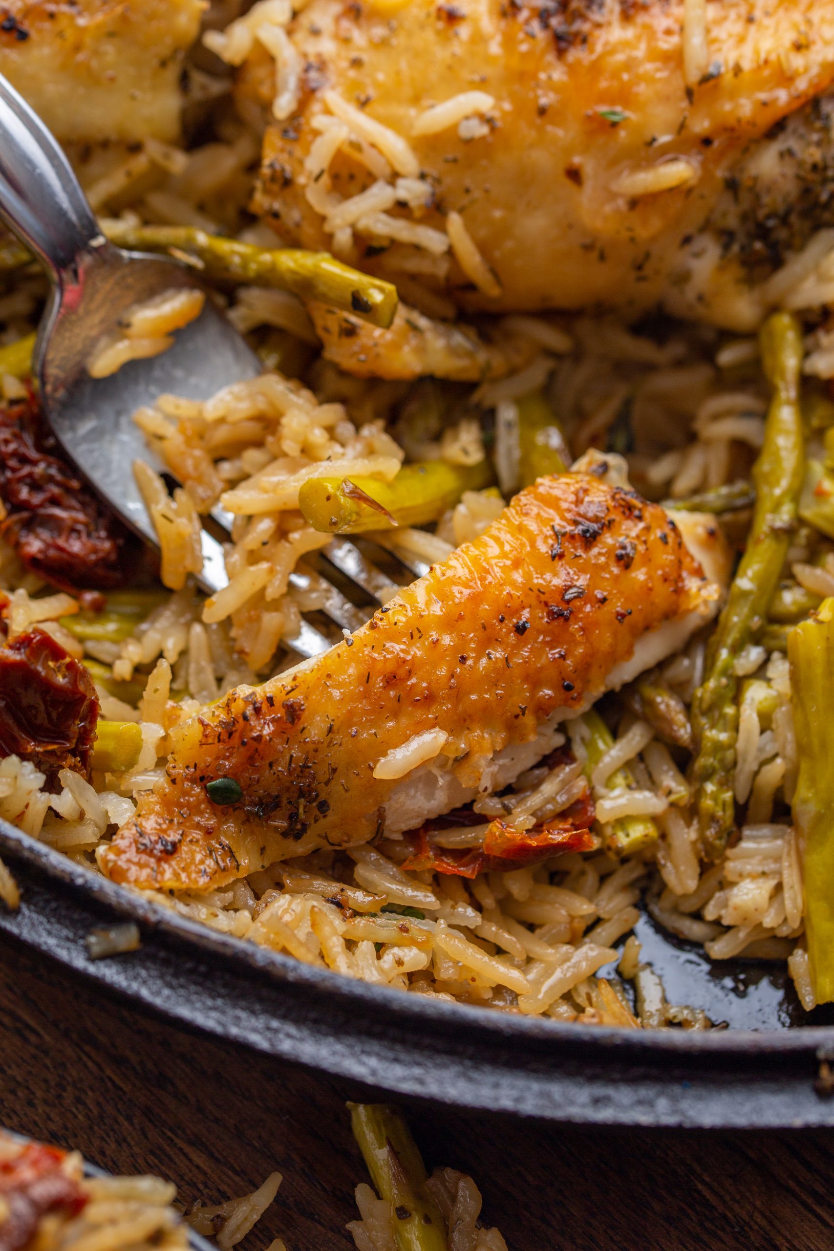 A cast-iron skillet filled with seasoned, roasted chicken thighs on a bed of rice mixed with green vegetables, garnished with thyme and lemon wedges.