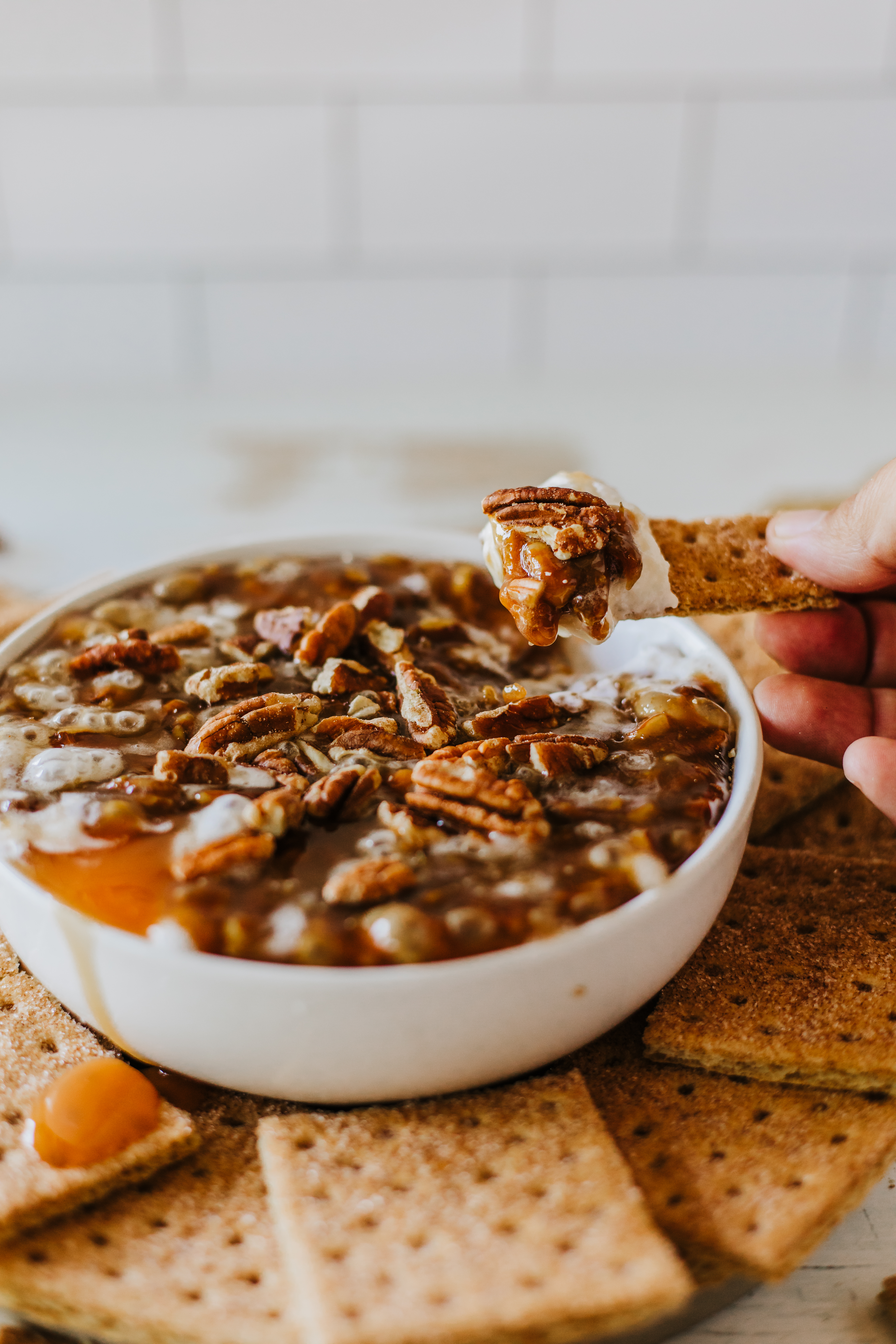 A bowl filled with No Bake Pecan Pie Dip with Cream Cheese surrounded by graham crackers. Two gold spoons are placed to the right.