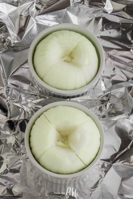 Two peeled and cored onions placed in white ramekins, set on a reflective foil surface.