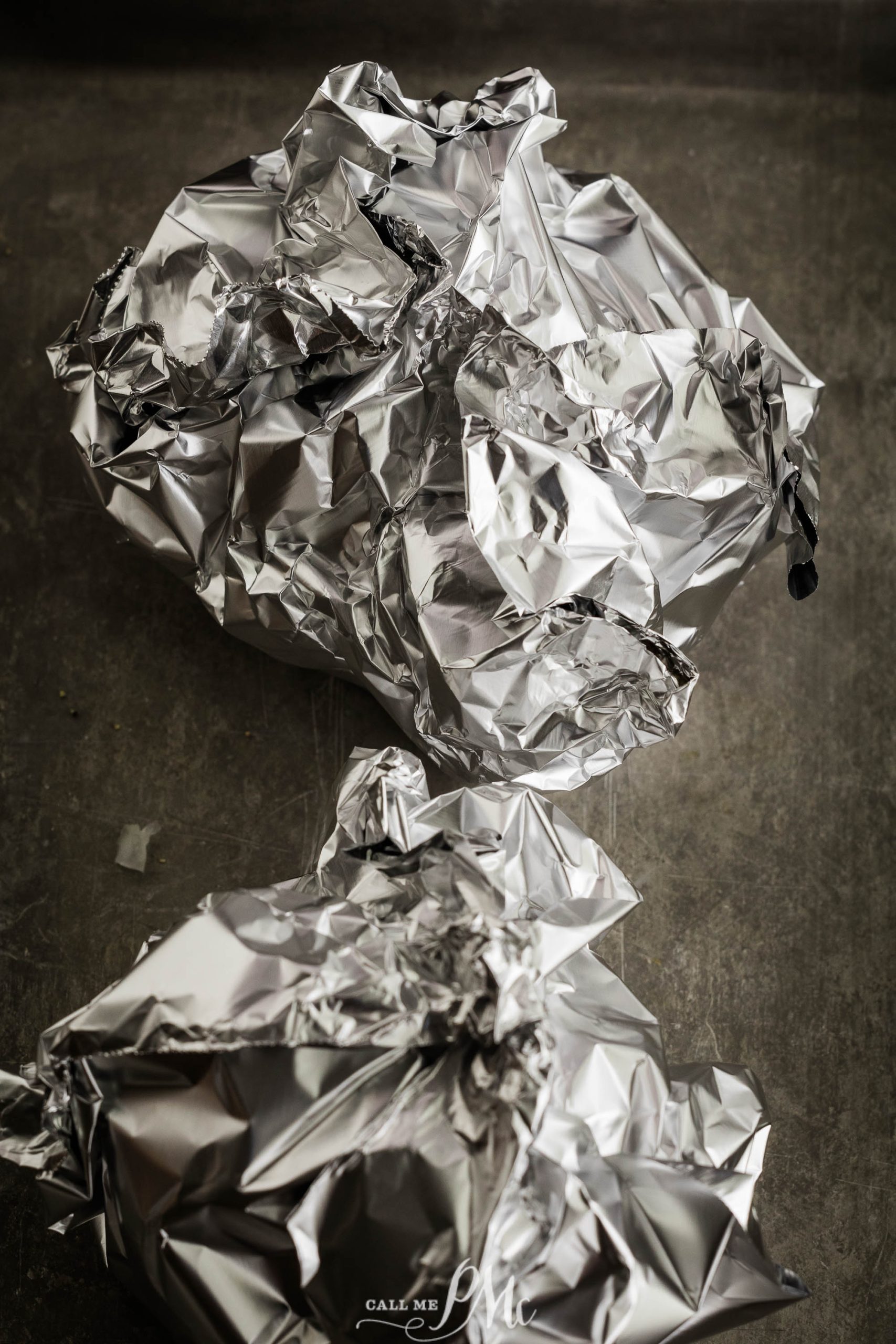 Wrinkled and balled-up pieces of aluminum foil lie on a gray surface.