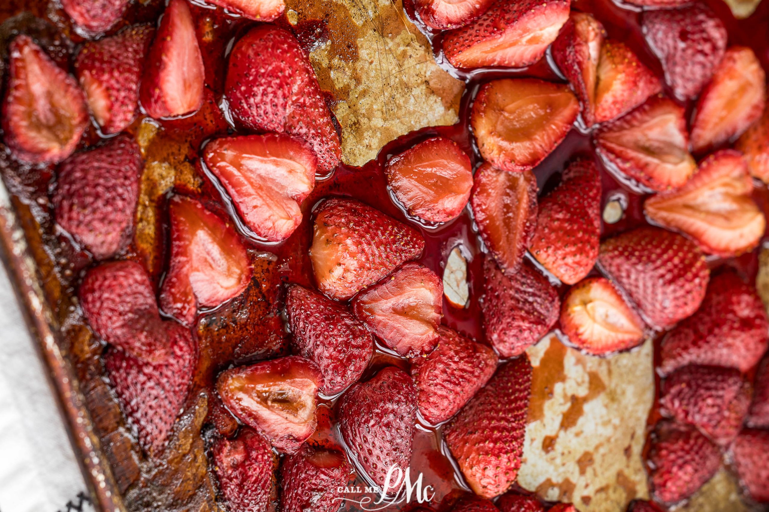 Roasted strawberries on a baking tray with a caramelized surface, showing a mix of whole and halved berries with visible juices.