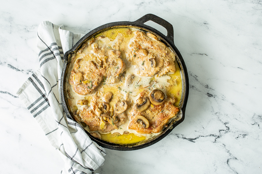 A cast iron skillet filled with creamy chicken and mushrooms on a marble countertop, accompanied by a striped kitchen towel.