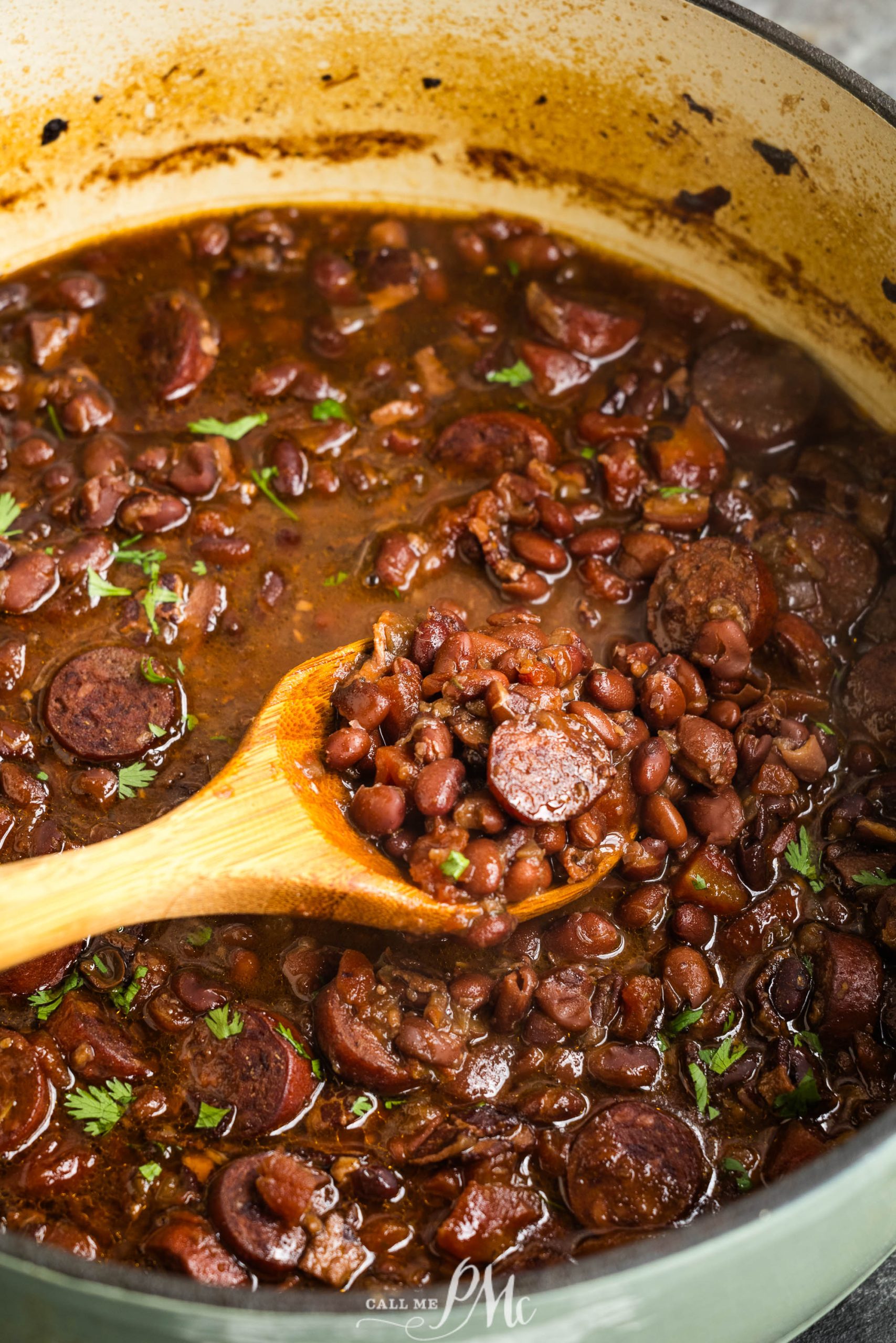 A pot of cooked soup & some chopped herbs on top, with a wooden spoon stirring the mixture.