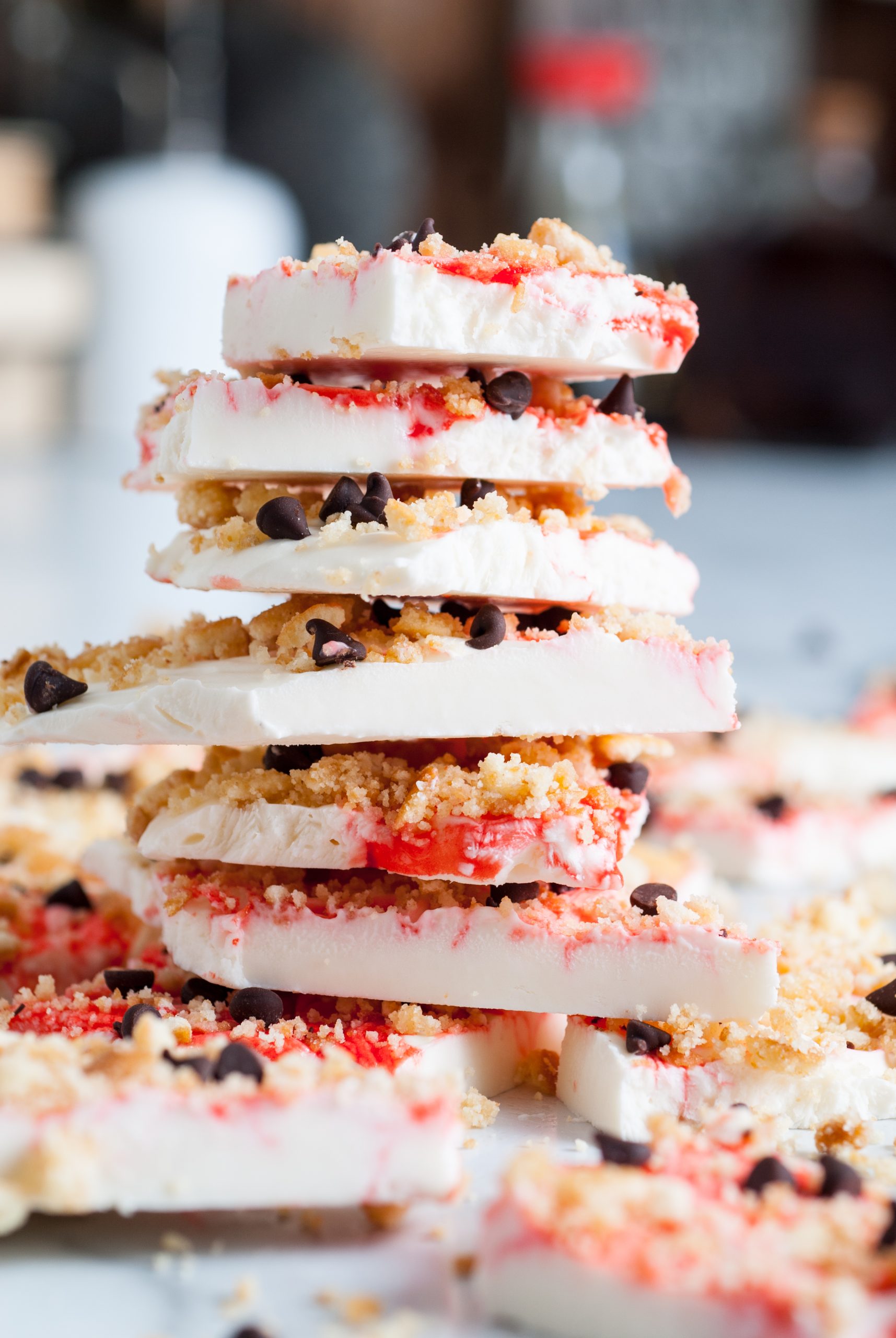 A stack of white chocolate bark pieces with red swirls, chocolate chips, and crumbly toppings.