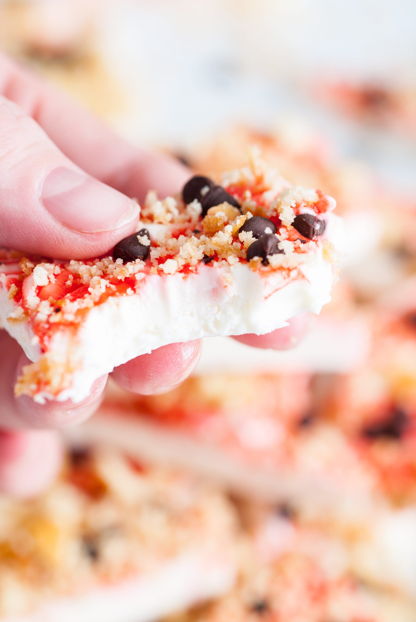 Hand holding a partially eaten piece of colorful yogurt bark topped with granola and chocolate chips.