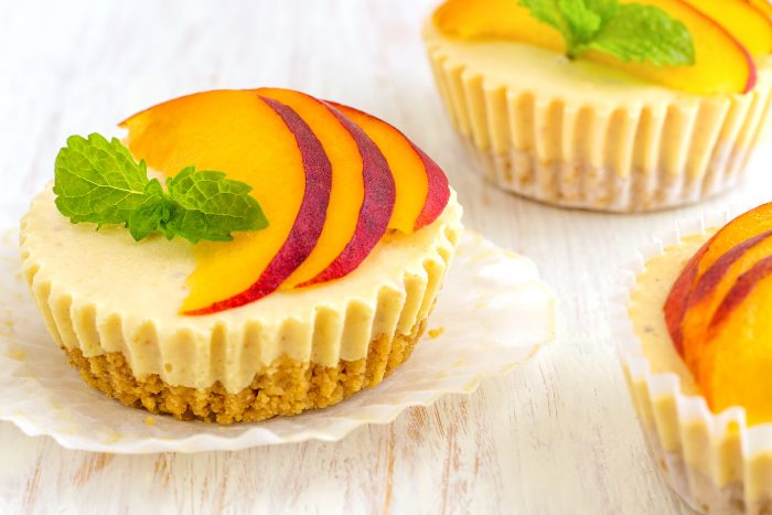 Peaches & Cream Greek Yogurt Cheesecake topped with peach slices and mint leaves on a wooden surface.