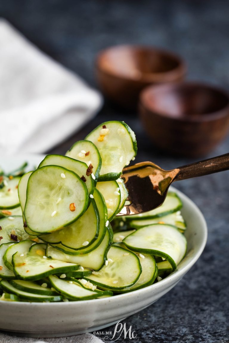 A bowl of sliced cucumber salad being lifted by a fork, with two wooden bowls in the background.