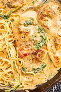 A close-up of creamy Tuscan chicken with pasta, featuring chicken breasts, spinach, sun-dried tomatoes, and a rich cream sauce.