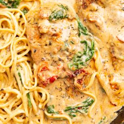 A close-up of creamy Tuscan chicken with pasta, featuring chicken breasts, spinach, sun-dried tomatoes, and a rich cream sauce.