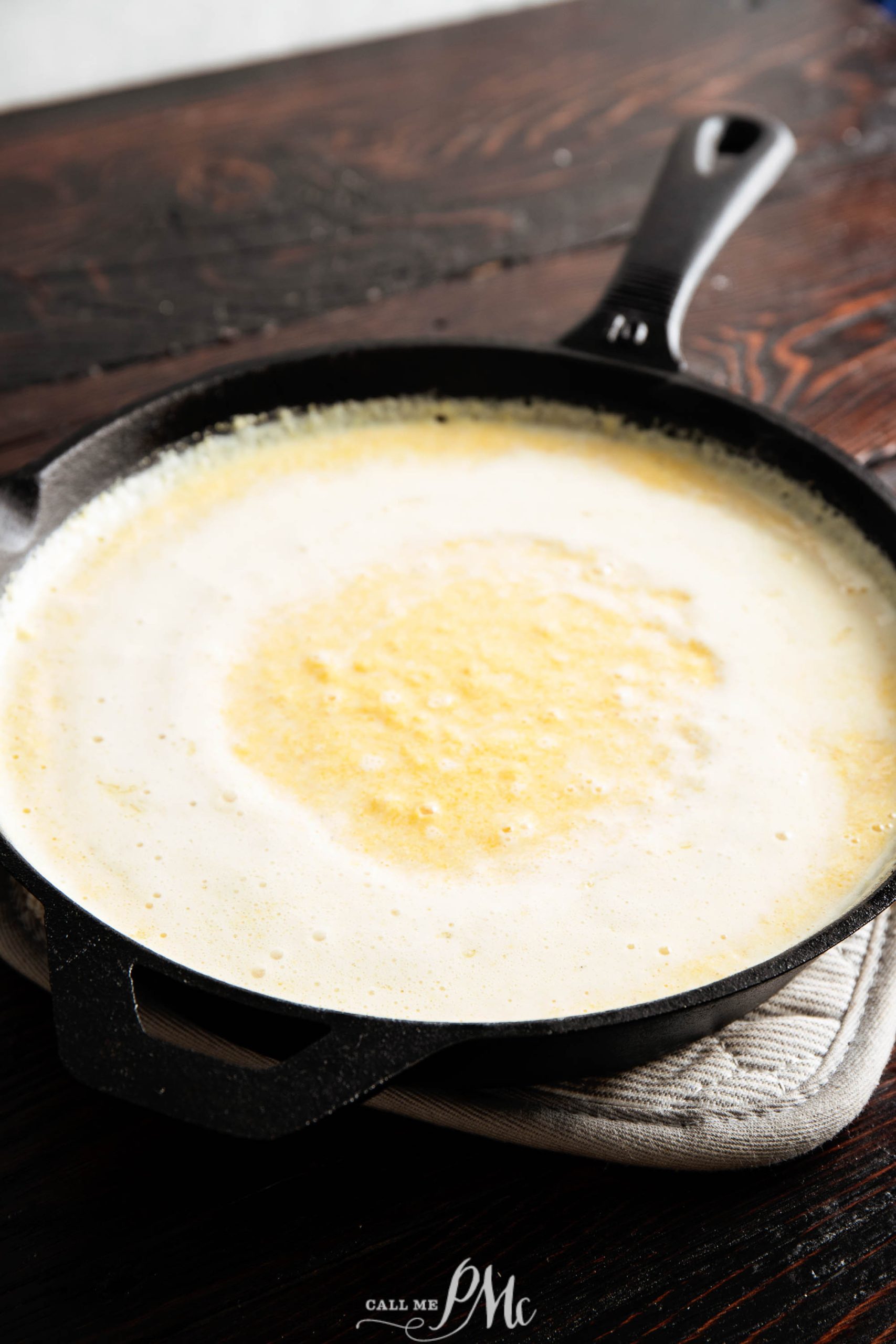 A cast iron skillet filled with a creamy, bubbling sauce on a wooden table.