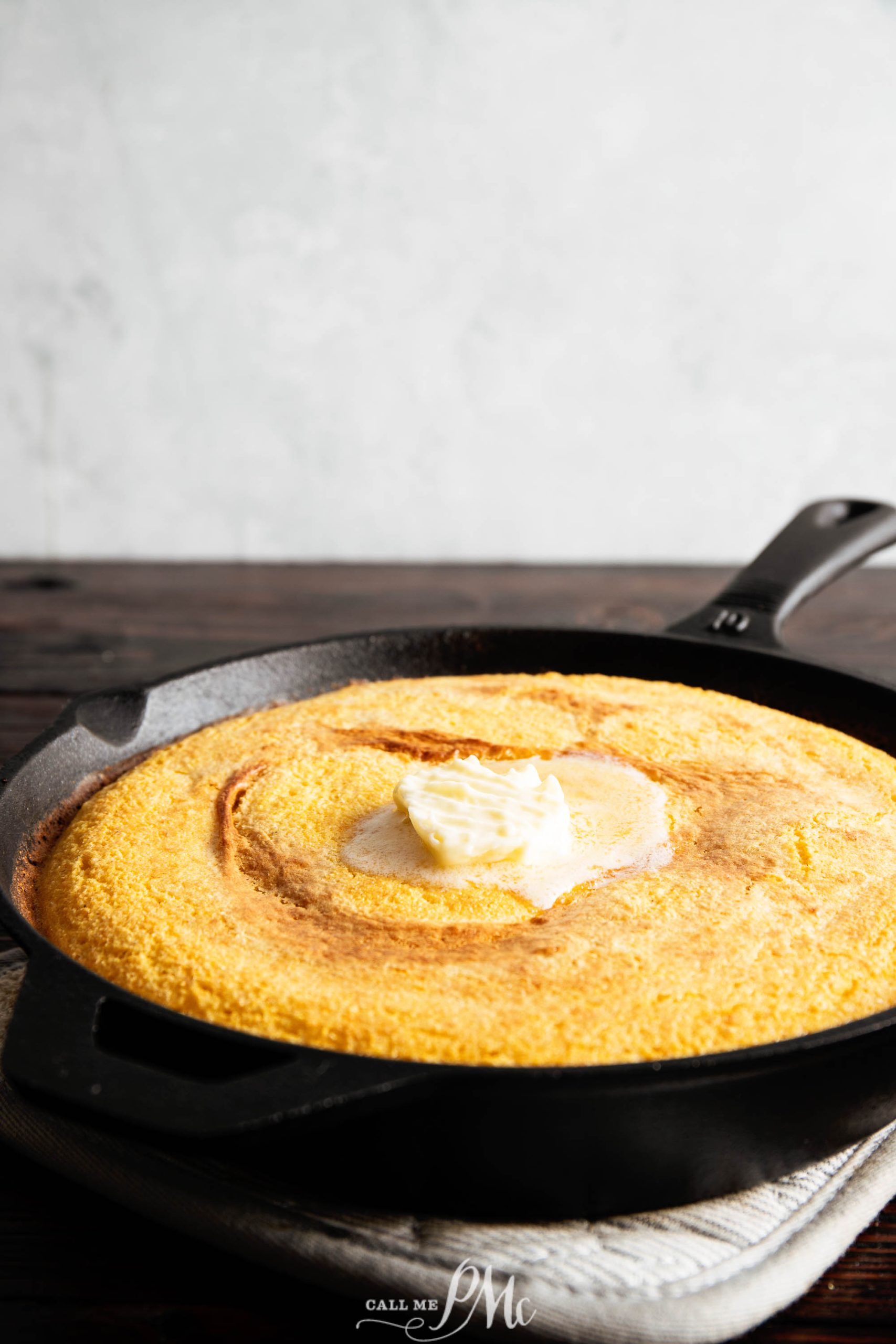 A cast iron skillet contains freshly baked cornbread with a dollop of butter melting in the center.