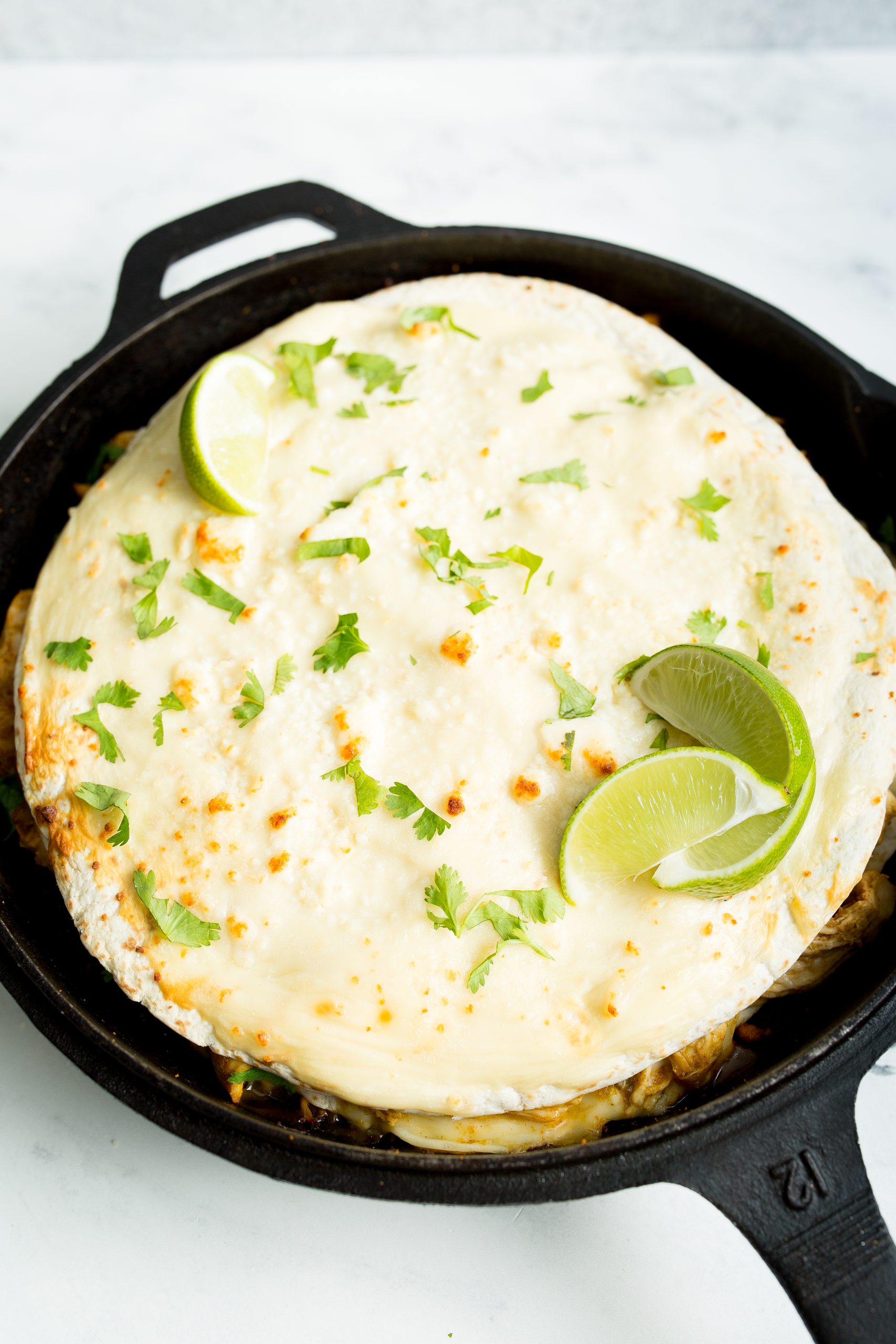 A round baked dish topped with melted cheese, green garnish, and lime wedges in a black cast iron skillet.