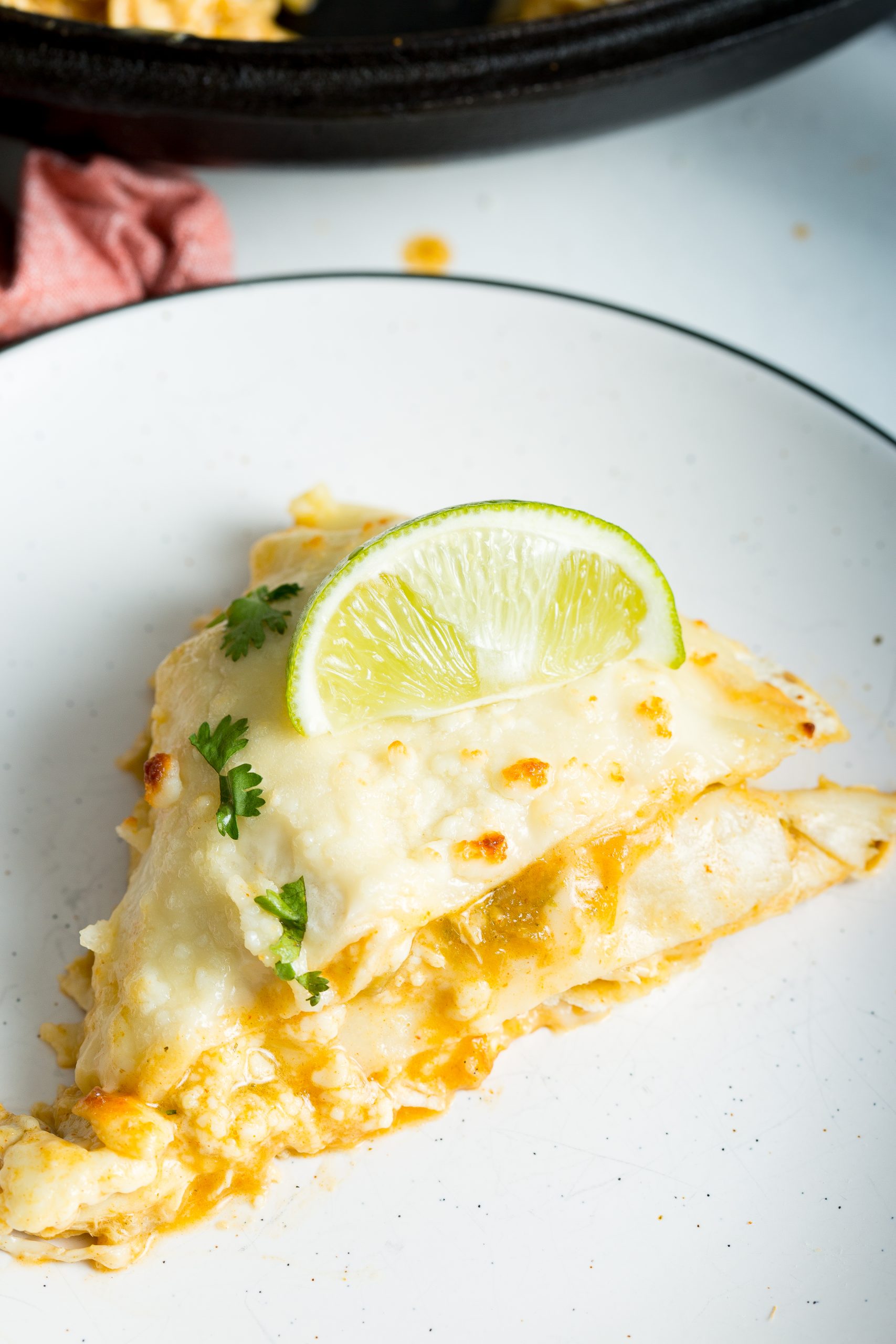 A serving of Mexican White Chicken Tortilla Lasagna with melted cheese, garnished with a slice of lime and a sprig of cilantro, on a white plate.