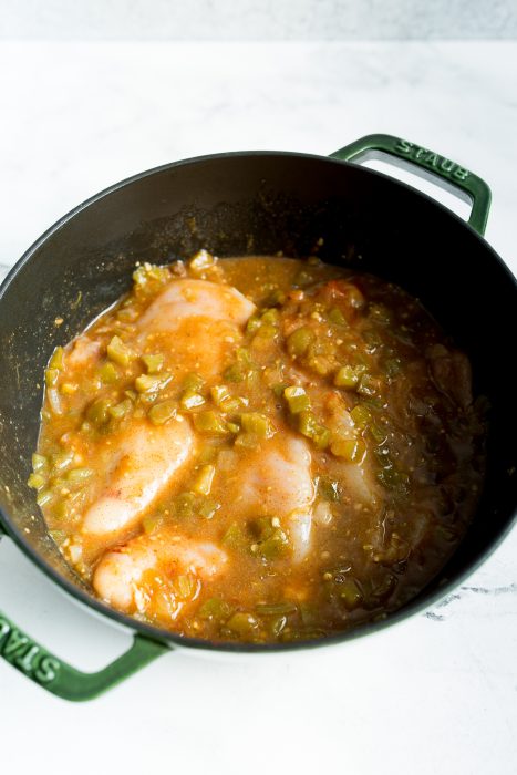 A pot filled with chicken breasts simmering in a sauce containing chopped green bell peppers and other seasonings.