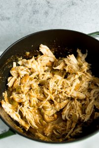 A pot filled with shredded chicken mixed with a savory green sauce, placed against a gray background.