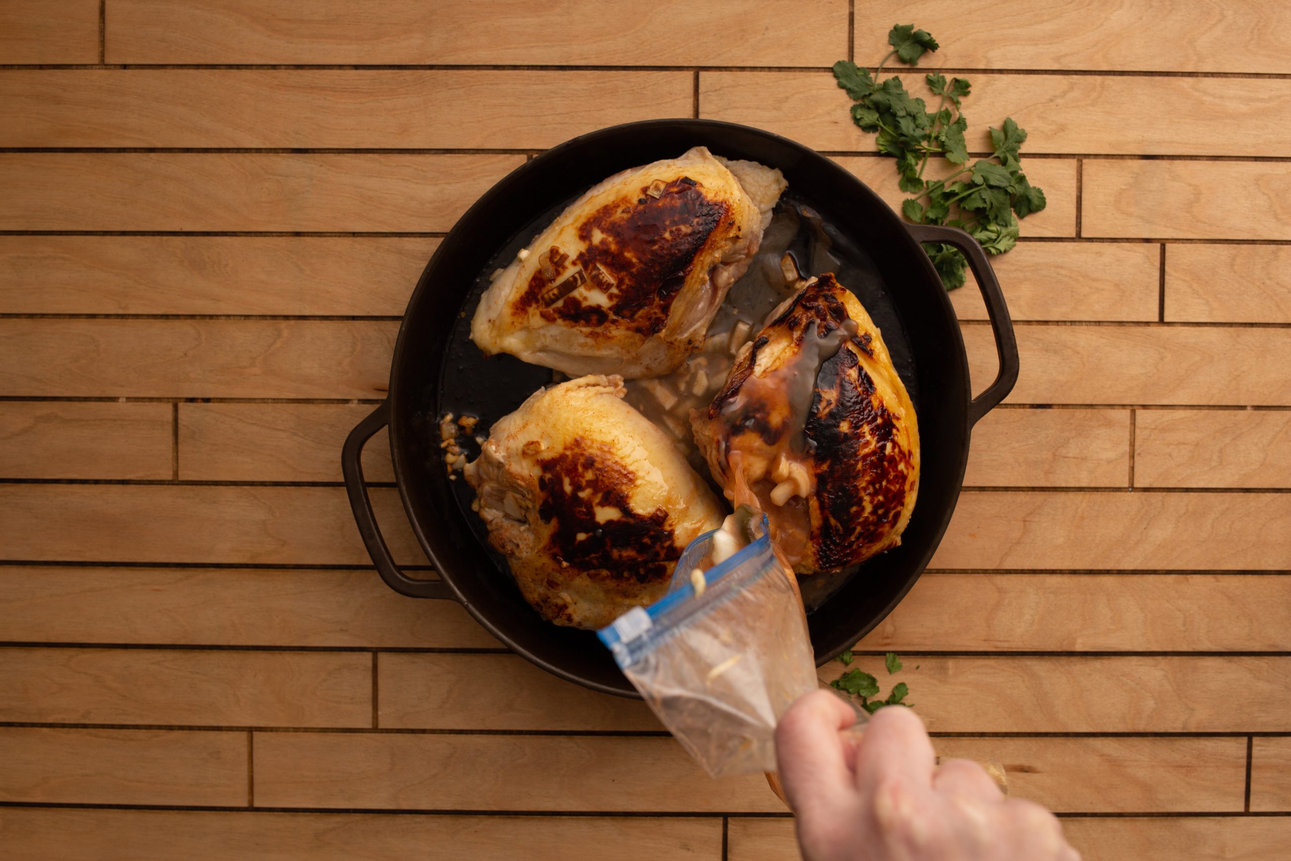 Three cooked chicken breasts with browned skin in a cast iron skillet, garnished with chopped herbs, on a wooden surface.