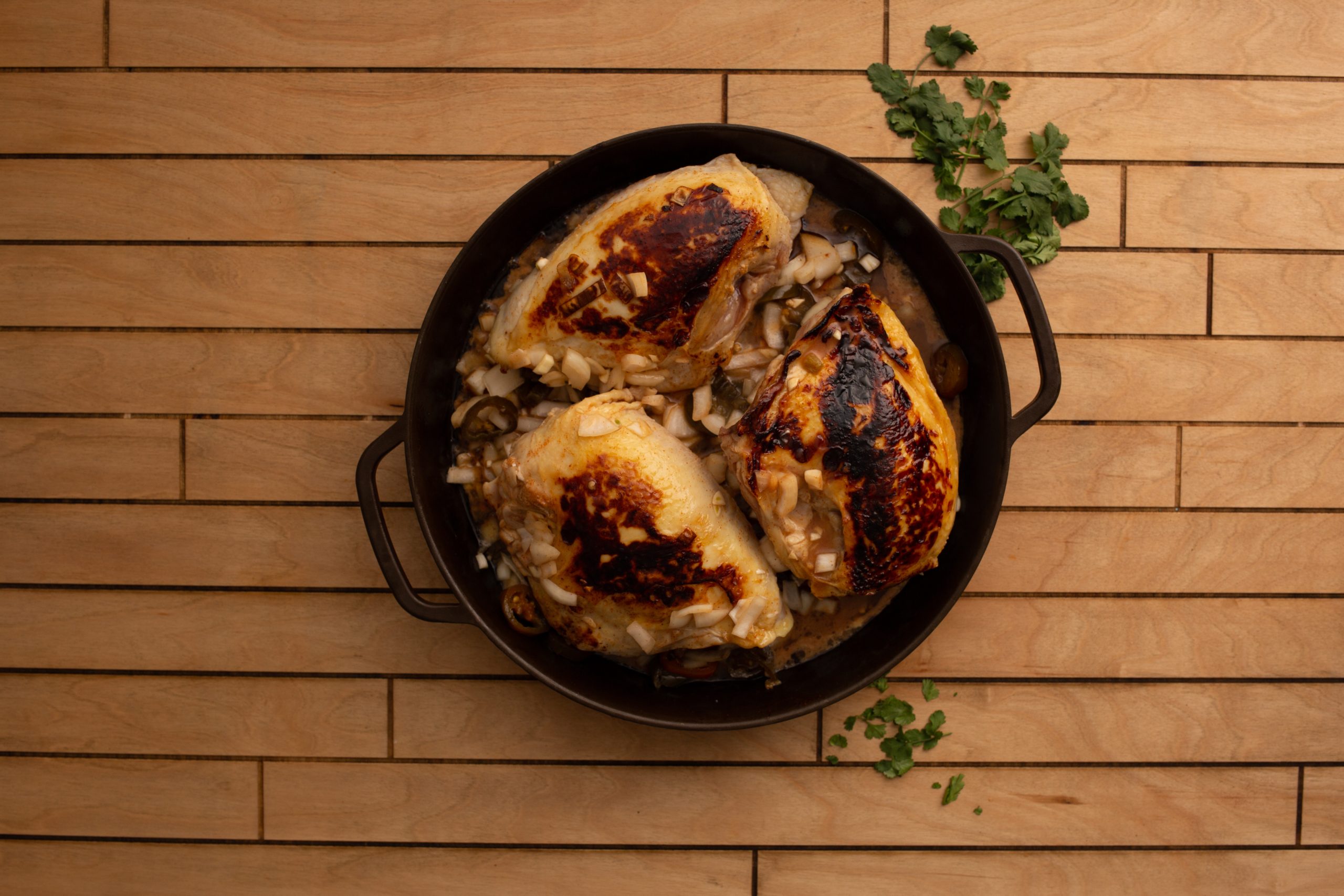 Chipotle Lime Split Breasts with browned skin in a cast iron skillet, garnished with chopped herbs, on a wooden surface.