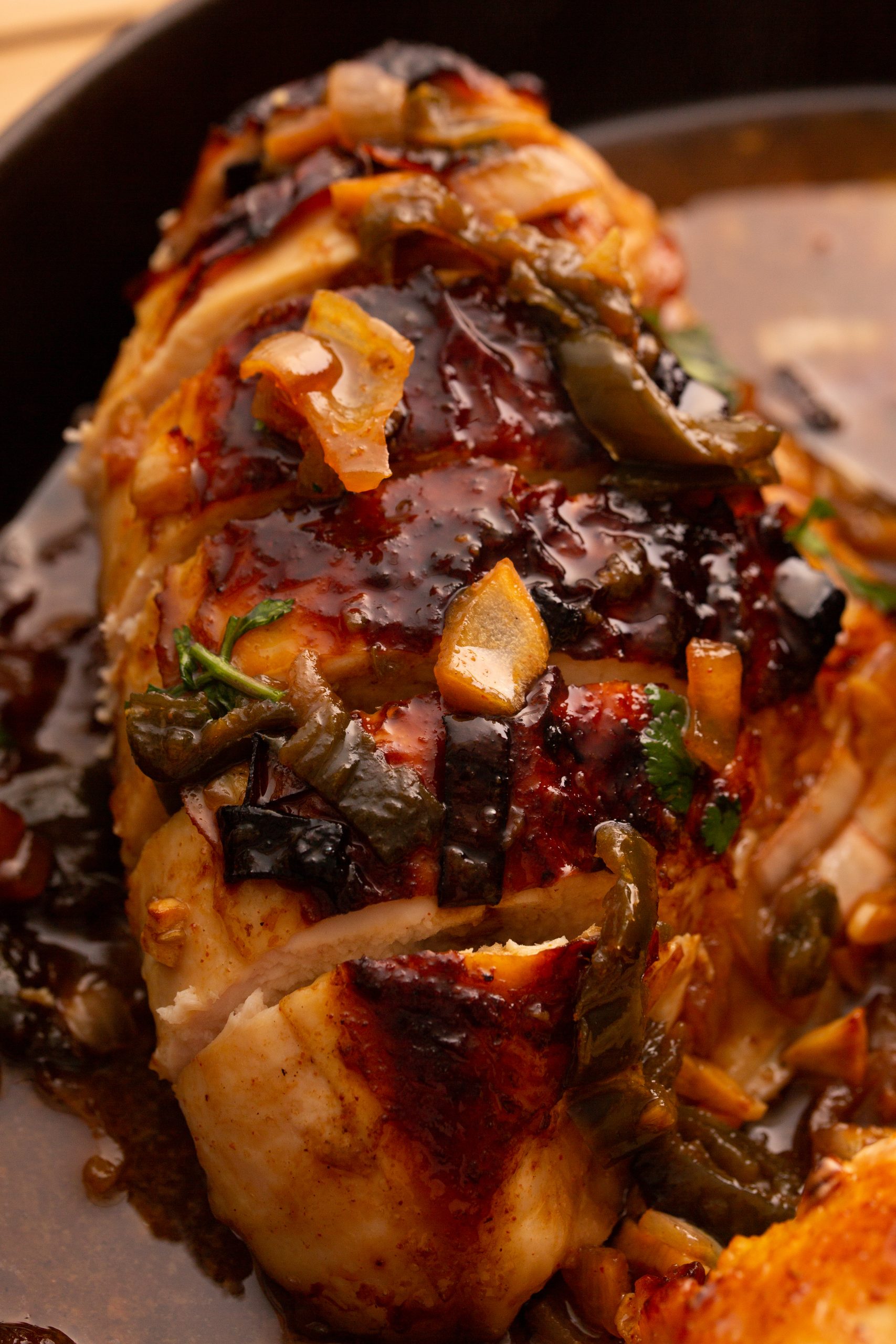 Close-up of a cooked stuffed chicken breast garnished with caramelized onions and vegetables in a brown sauce. The chicken is sliced, revealing the stuffing inside.