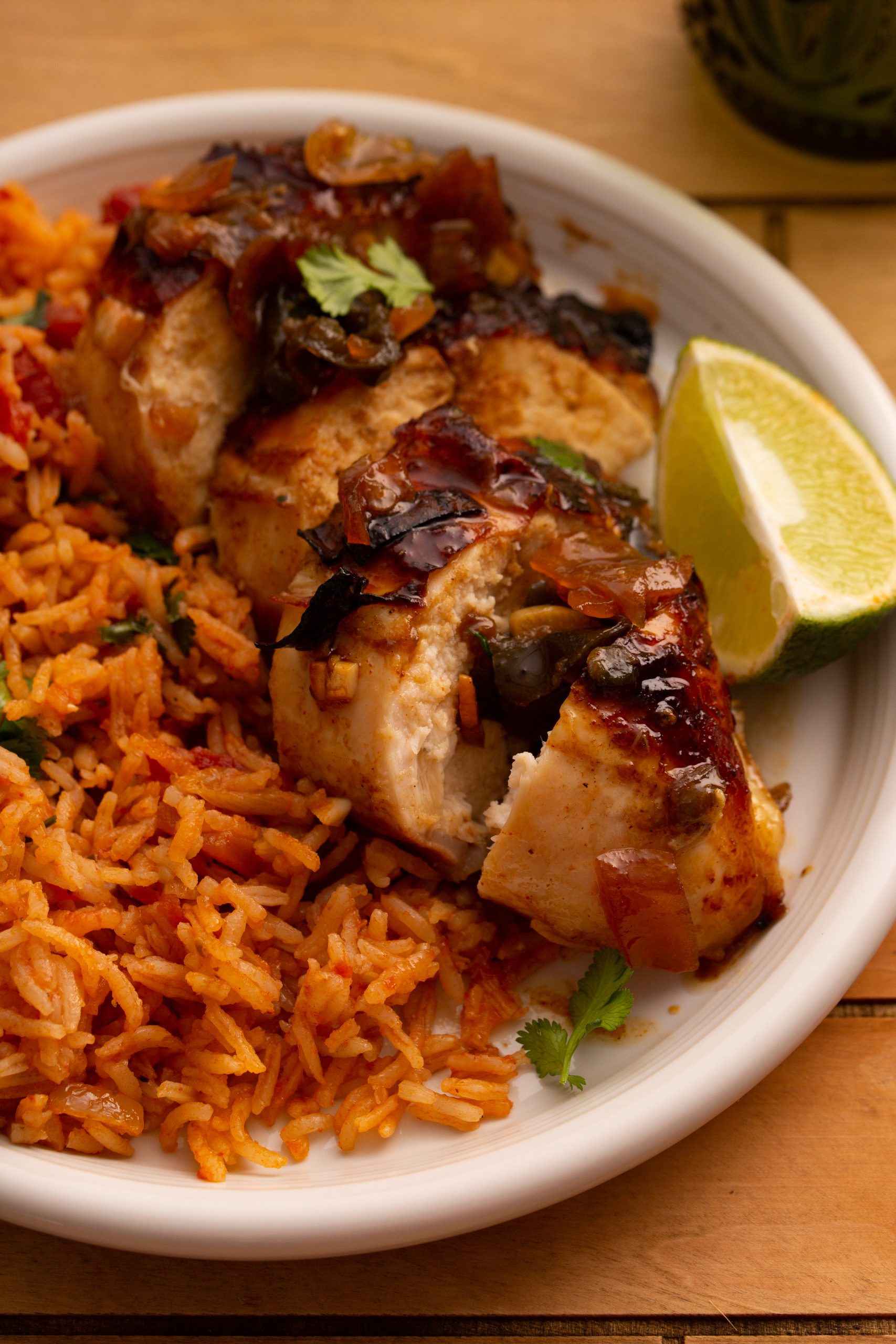 A plate of seasoned rice served with sliced Chipotle Lime Split Breasts topped with onions and a lime wedge on the side.