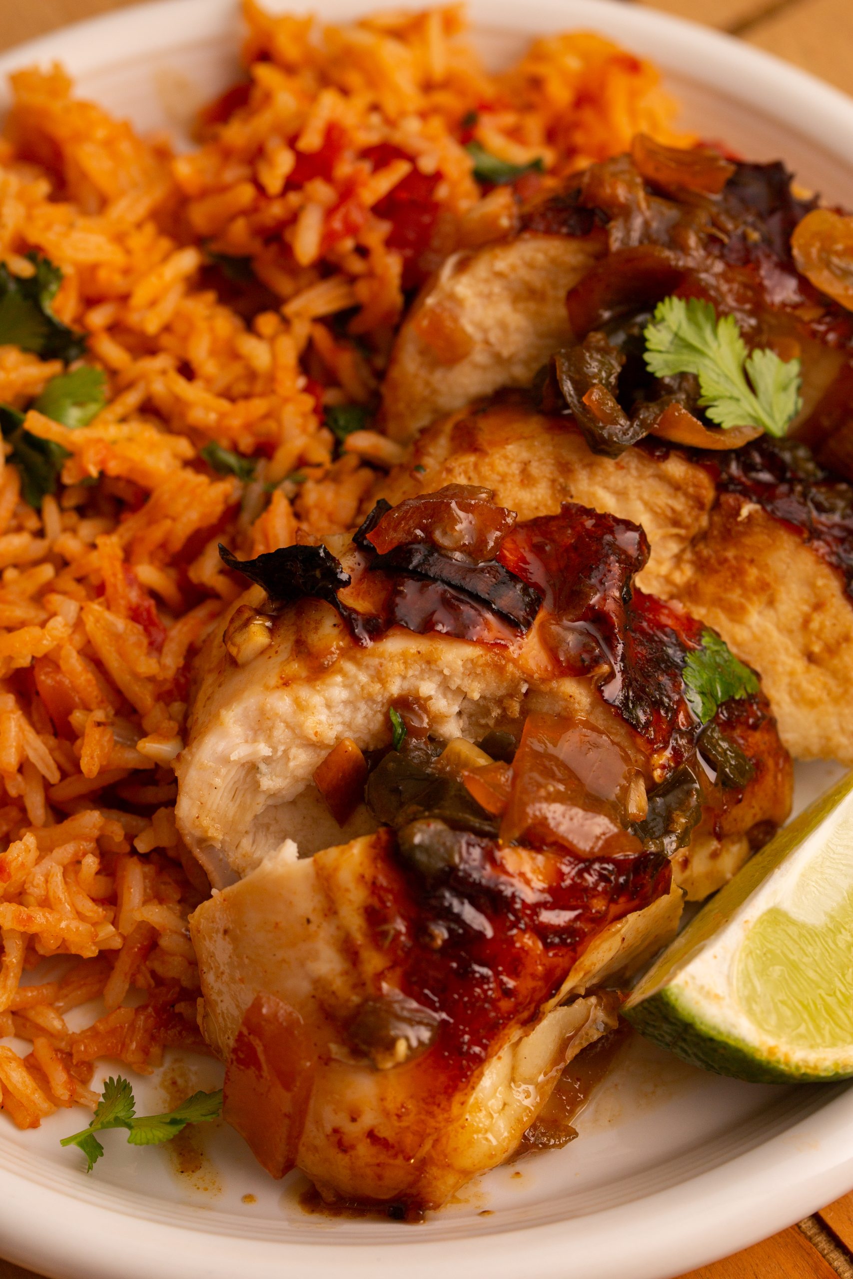 A plate of Chipotle Lime Split Breasts with a spicy glaze, garnished with cilantro and served with a side of seasoned rice and a lime wedge.