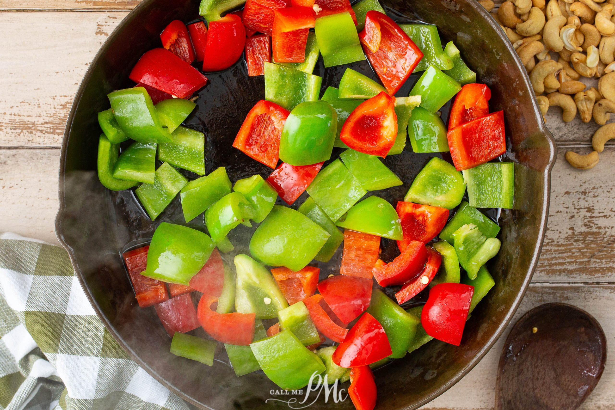 A cast iron skillet filled with chunks of red and green bell peppers being sautéed. A checked cloth is partially visible on the left.