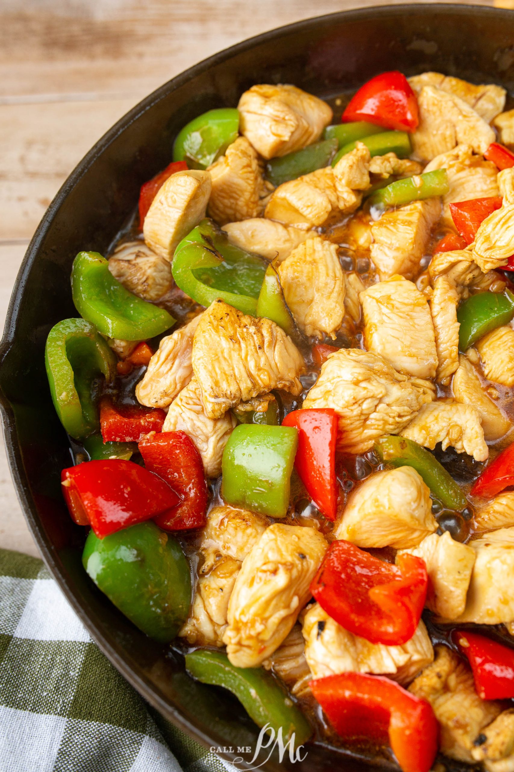 A close-up of a skillet containing cooked chicken pieces, red bell peppers, and green bell peppers. The chicken and vegetables are mixed and appear to be seasoned.