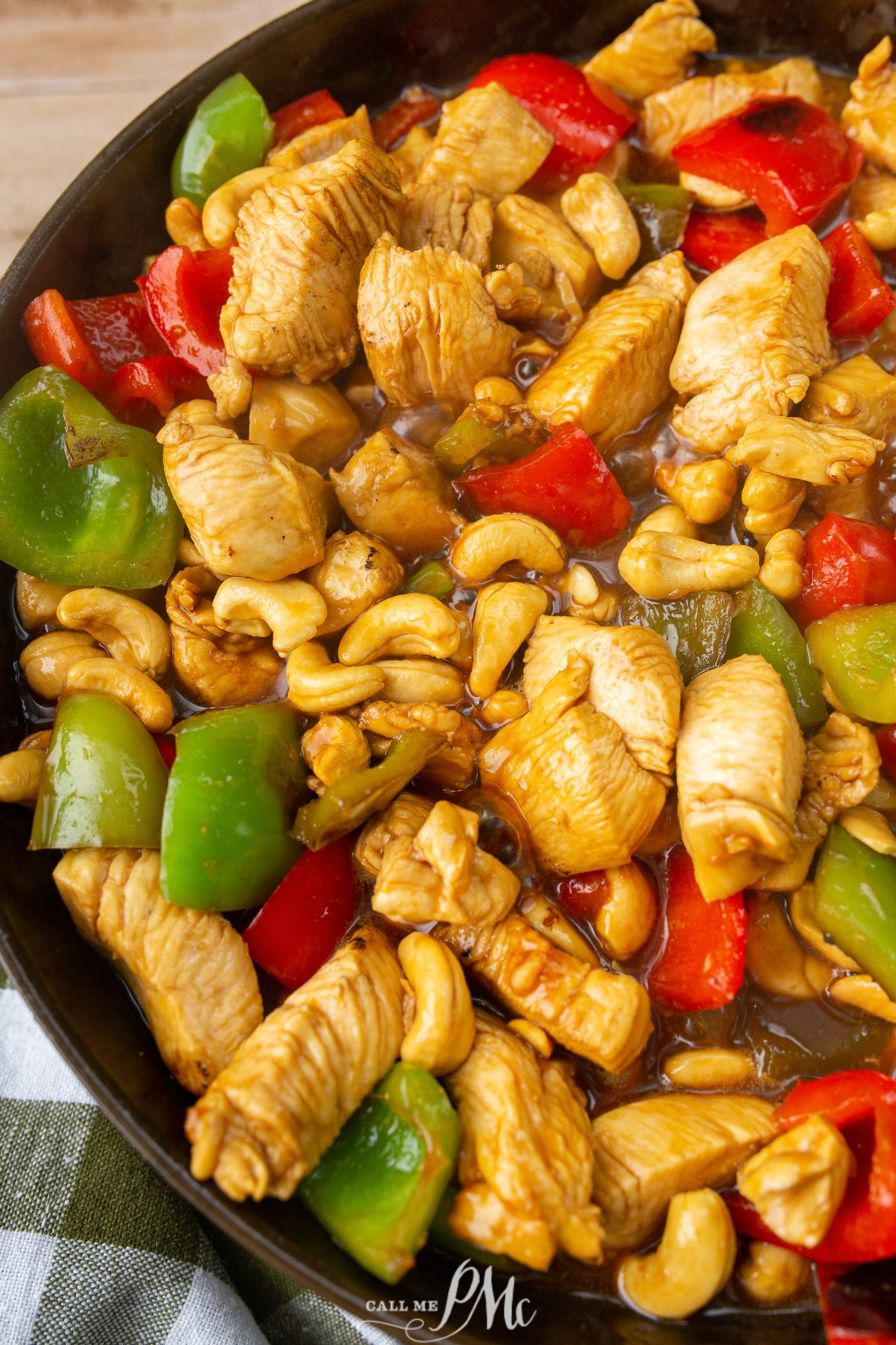 A skillet filled with cooked chicken pieces, green and red bell peppers, and cashews in a sauce.