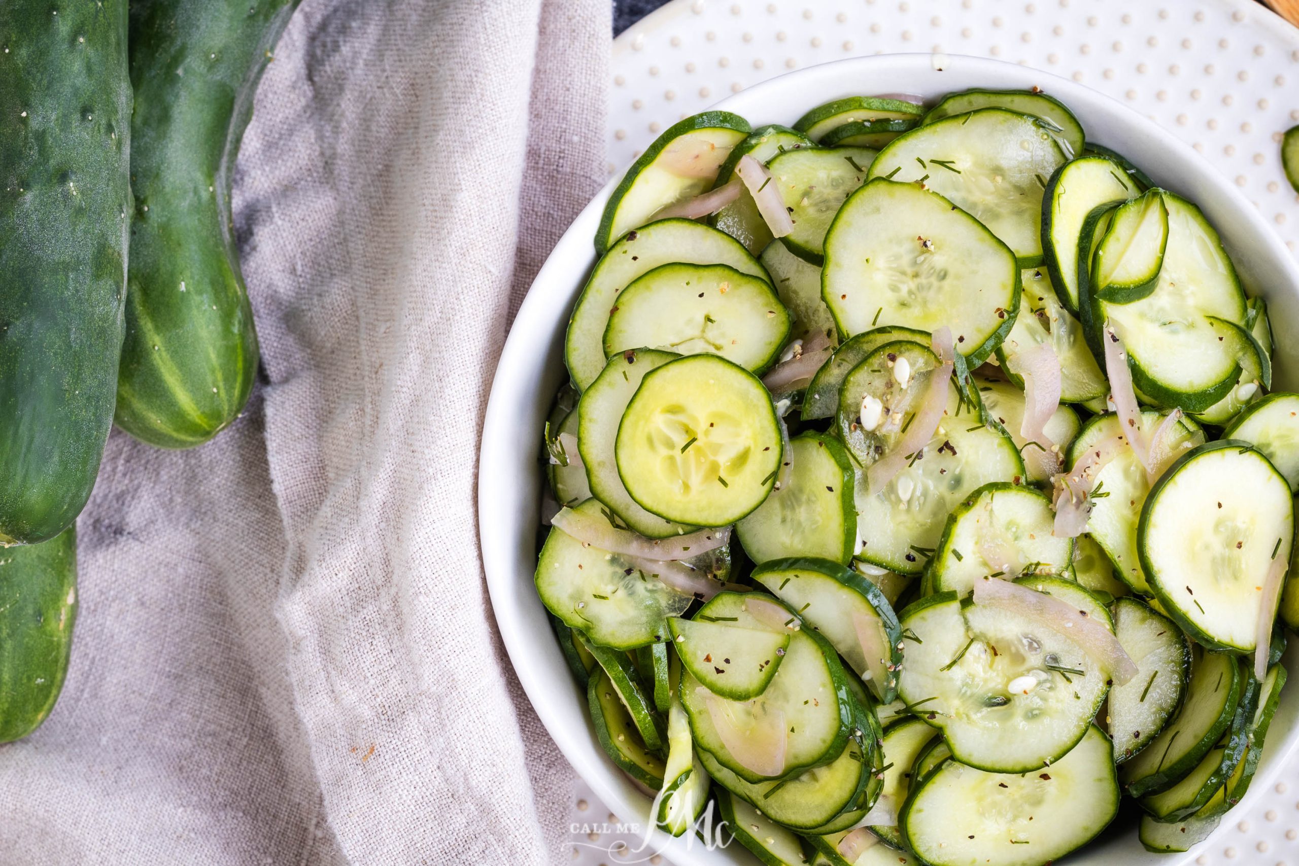 A white bowl filled with sliced cucumber salad recipe mixed with thinly sliced onions and garnished with herbs.