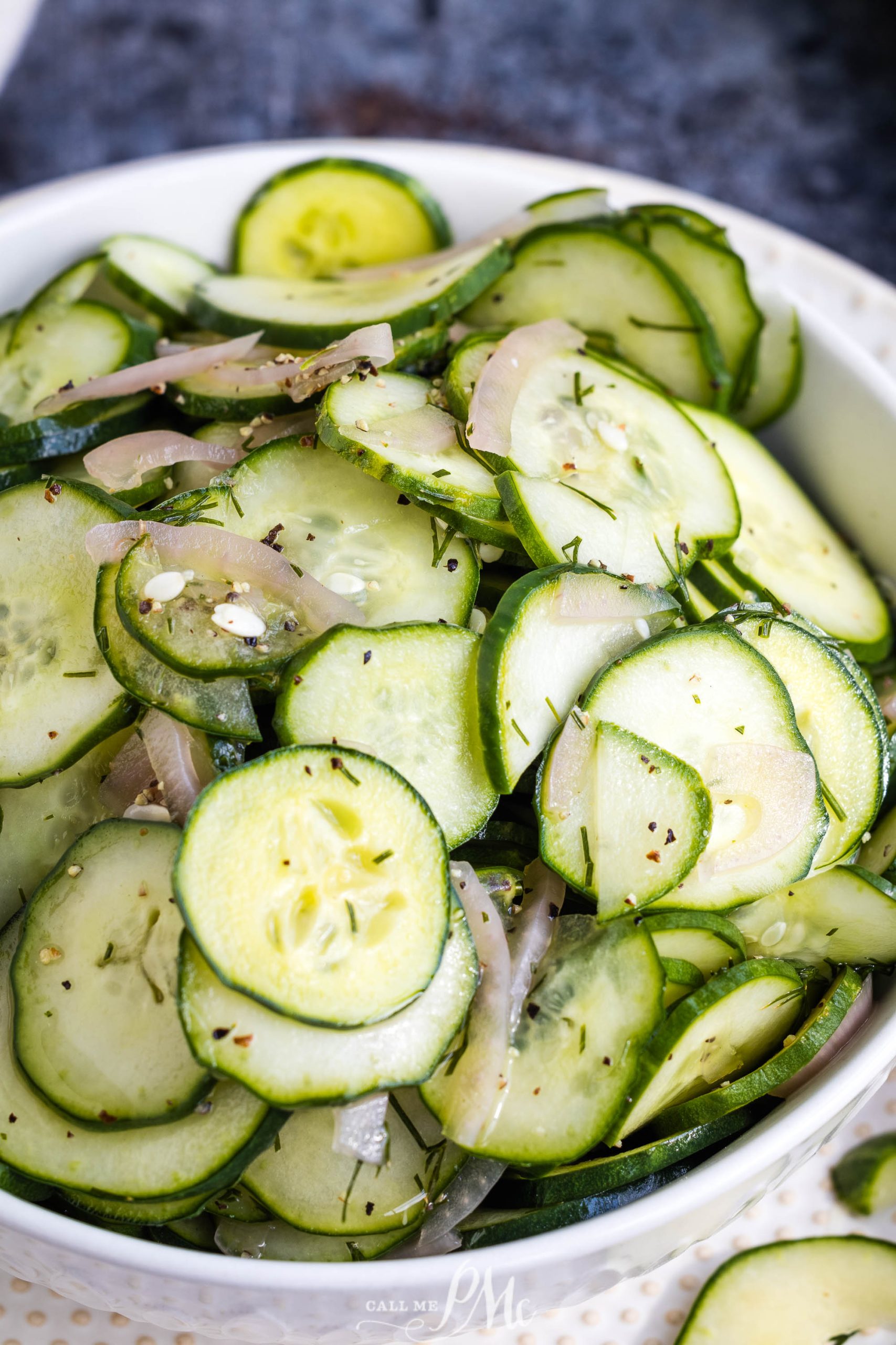 A white bowl filled with sliced cucumber salad recipe mixed with thinly sliced onions and garnished with herbs.