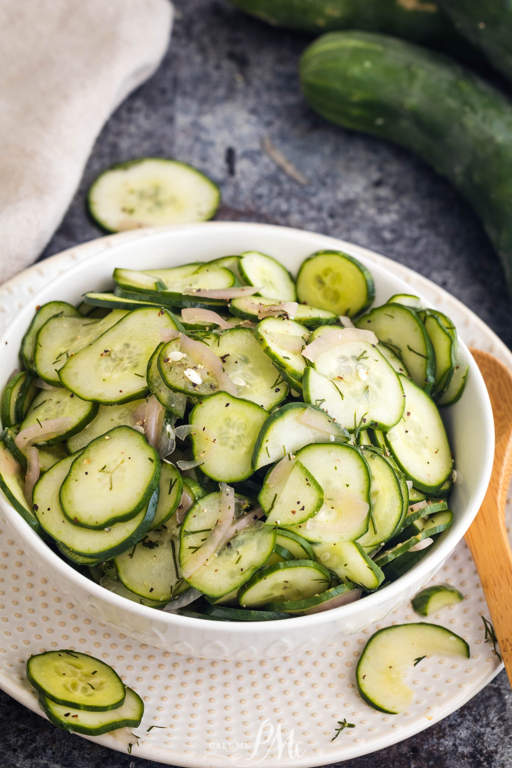 A white bowl filled with sliced cucumber salad recipe mixed with thinly sliced onions and garnished with herbs.