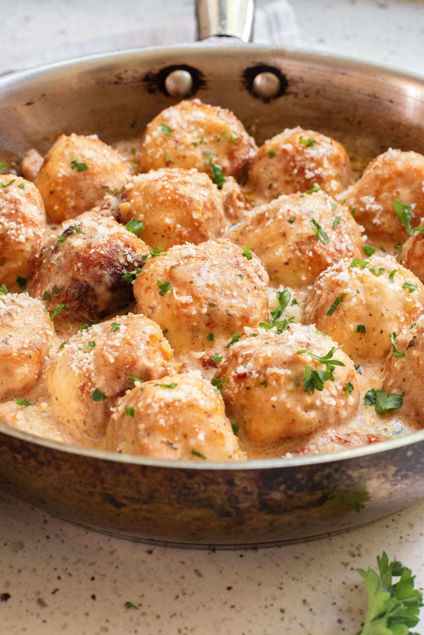 A skillet filled with golden-brown meatballs topped with creamy sauce and garnished with chopped parsley.