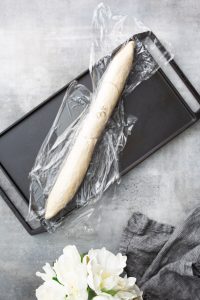 A wrapped dough roll marked "35" lies on a black tray. A gray cloth and white flowers are visible in the foreground.