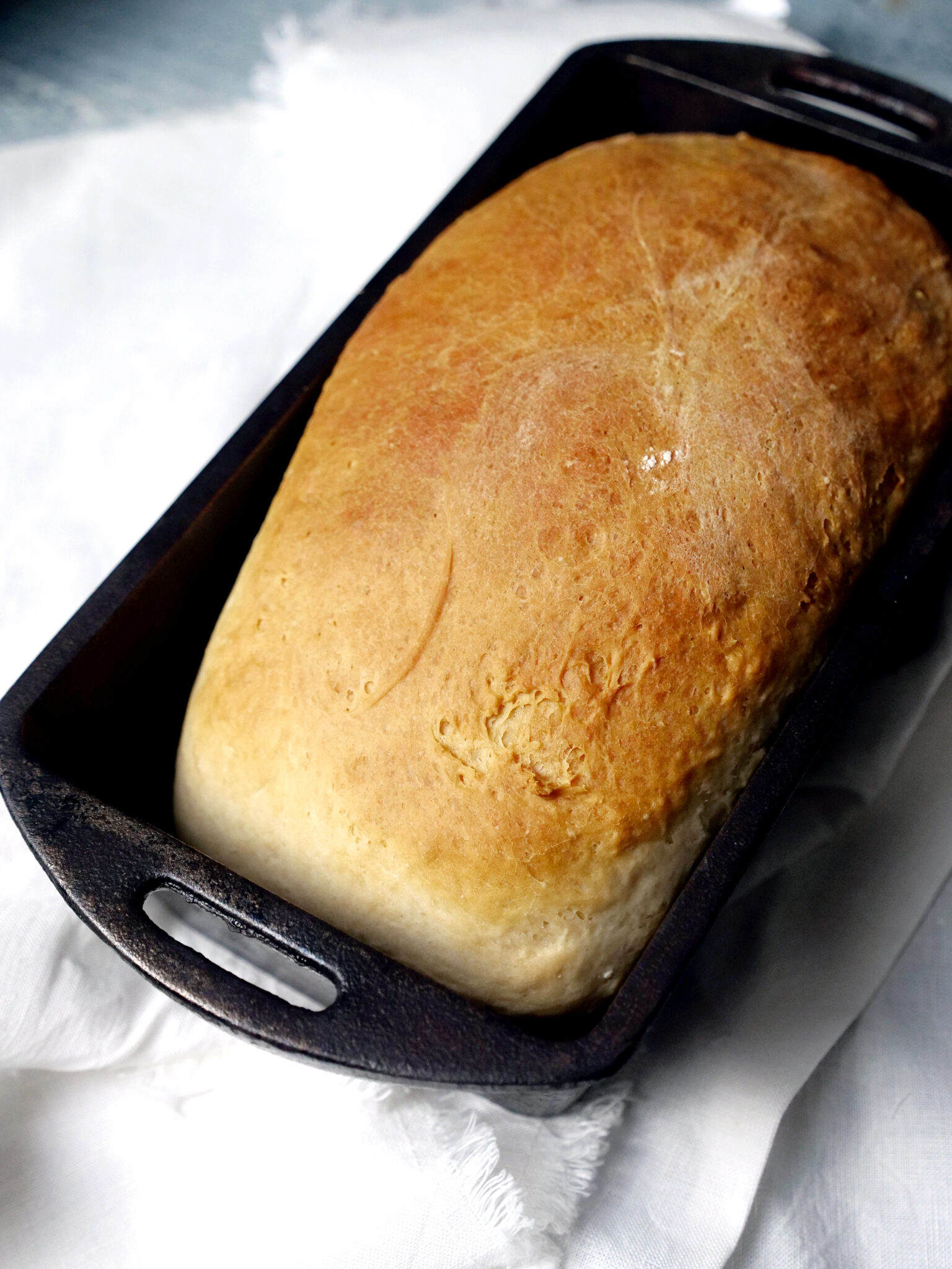 A loaf of bread in a black rectangular baking pan on a white cloth.