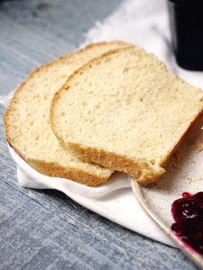 Two slices of white bread are placed on a white cloth next to a dish of red jam on a blue wooden surface.