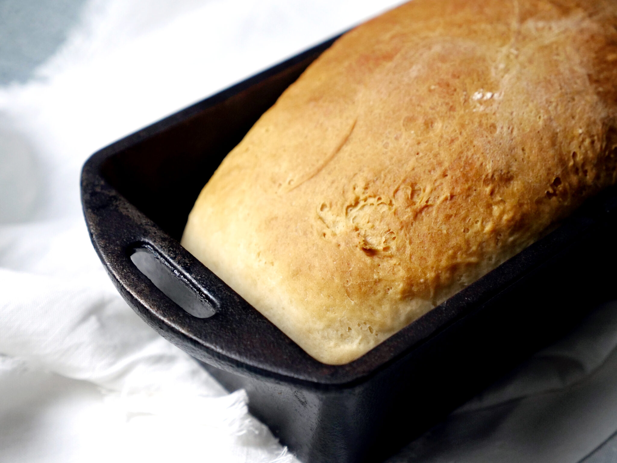 A freshly baked loaf rests in a black metal pan on a white surface.