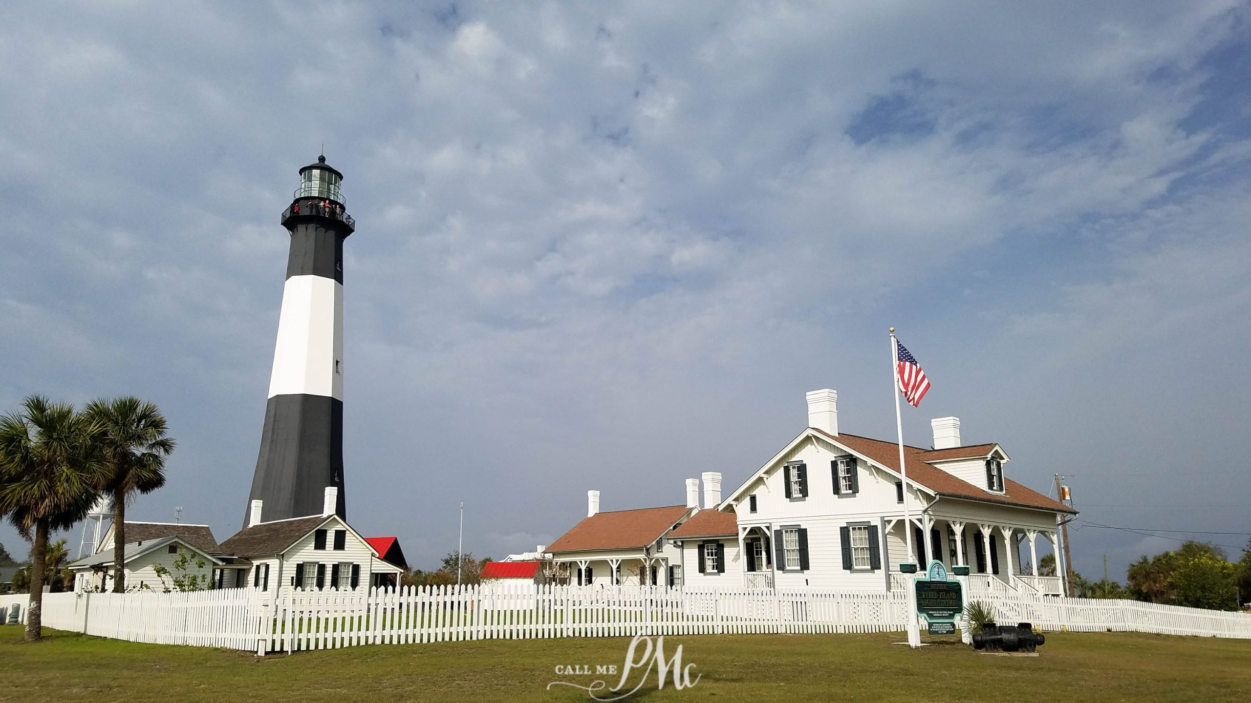 48 hours in Savannah. A black and white striped lighthouse stands next to a white house with a red roof, surrounded by a white picket fence under a partly cloudy sky. An American flag is displayed outside the house.