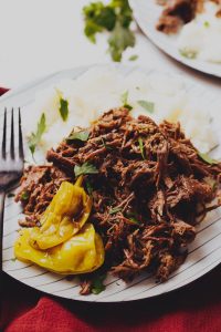 A plate of shredded beef garnished with yellow peppers and parsley, served with mashed potatoes.