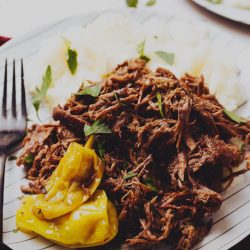 A plate of shredded beef garnished with yellow peppers and parsley, served with mashed potatoes.