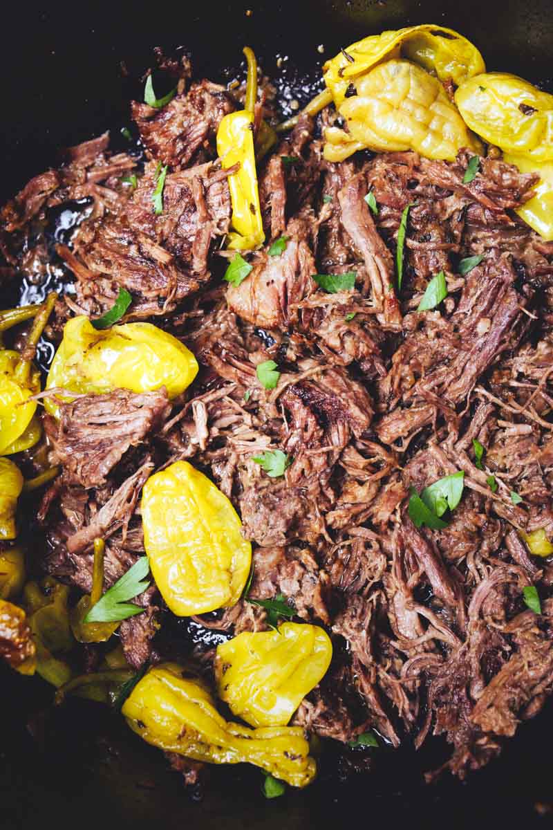 Dutch Oven Mississippi Pot Roast with yellow peppers and parsley garnish in a black dish.