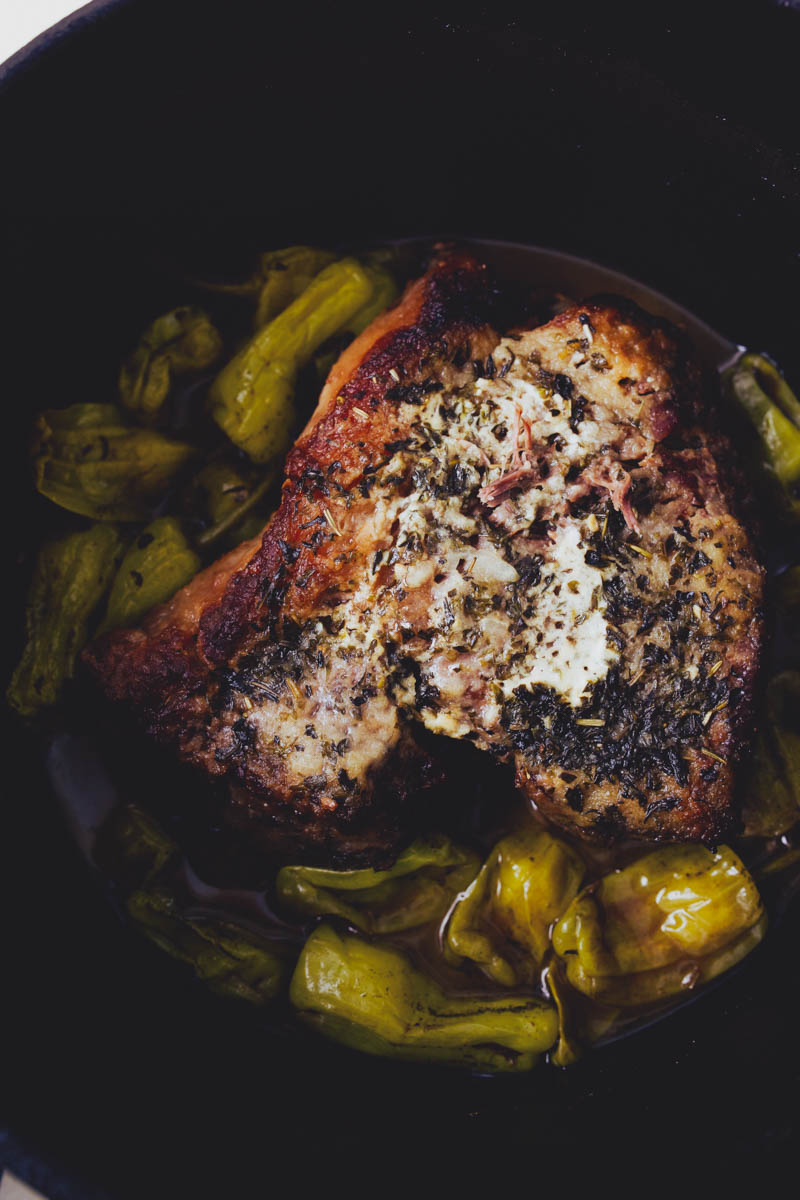 Close-up of a cooked, herb-crusted chicken breast garnished with green peppers in a dark dish.