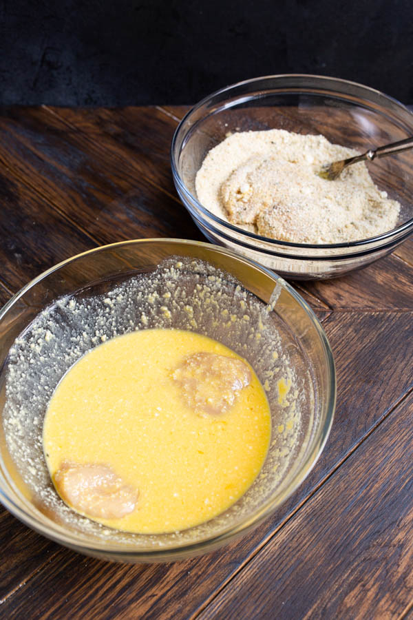 Two bowls on a wooden surface: one containing a yellow batter mixture and the other filled with breadcrumbs.