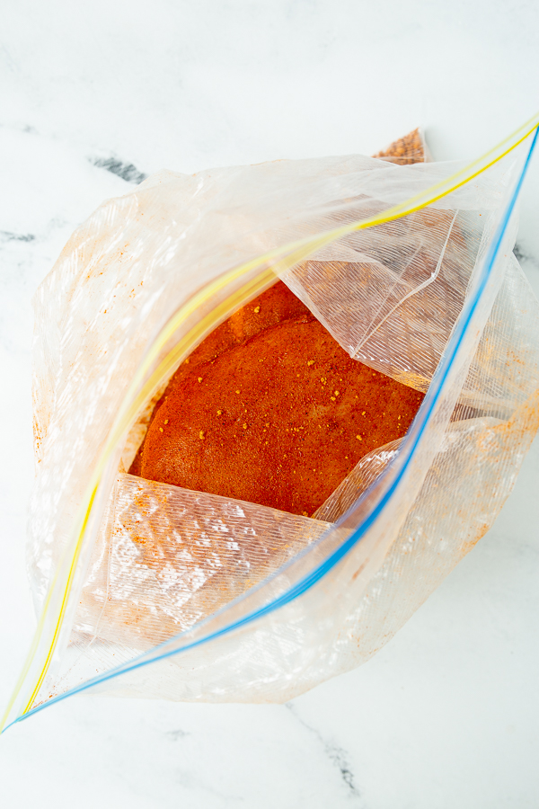 Plastic zipper bag filled with orange seasoning powder, placed on a white marble surface.