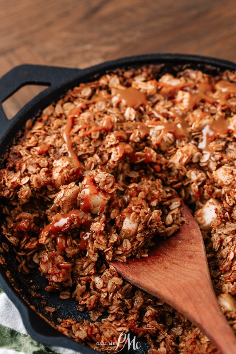 A close-up of a baked dish in a cast iron skillet, with a wooden spoon stirring a mixture that appears to be an oatmeal-based recipe drizzled with a sauce.