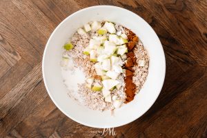 A bowl containing oats, milk, diced green apples, and a sprinkling of cinnamon on a wooden table.