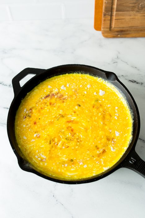 A cast iron skillet on a marble countertop containing partially cooked scrambled eggs.